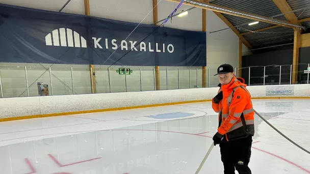 Henkilö huomiotakissa jääkiekkokaukalossa, taustalla Kisakallion logo.