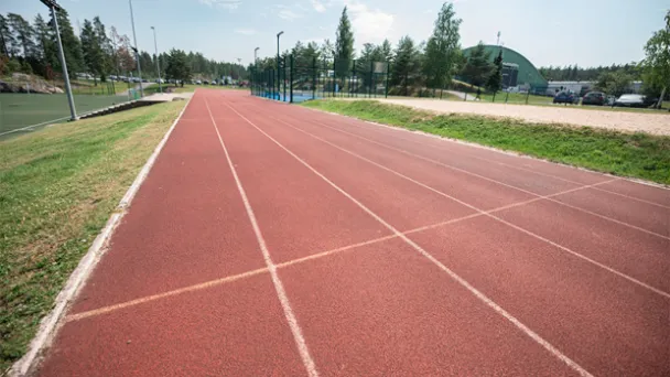 Punainen juoksurata, taustalla puita ja sininen taivas.