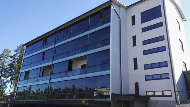 Kerrostalo, jossa on lasiseinä ja parkkitila alhaalla, kirkkaassa auringonpaisteessa.