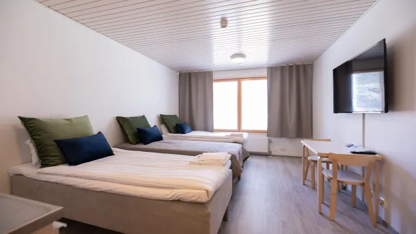 Kaksi vuodetta, pöytä, tuolit ja televisio vaaleassa huoneessa.