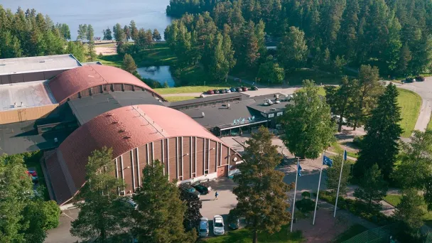 Punakattoinen rakennus vehreässä ympäristössä, taustalla järvimaisema.