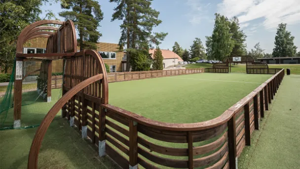 Suljettu nurmikenttä, puukaiteet, taustalla puita ja rakennuksia.