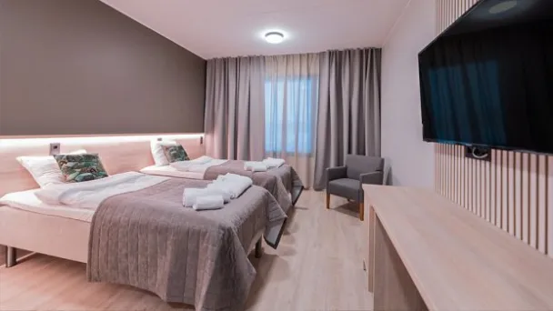 Hotellihuone, kaksi vuodetta, televisio, harmaat sävyt.