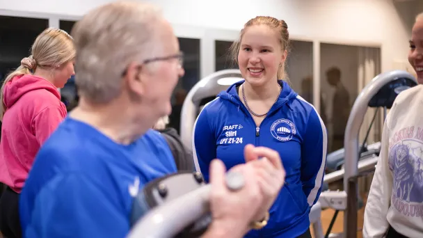 Kuntosalilla treenaava vanhempi mies keskustelee kahden naisen kanssa.