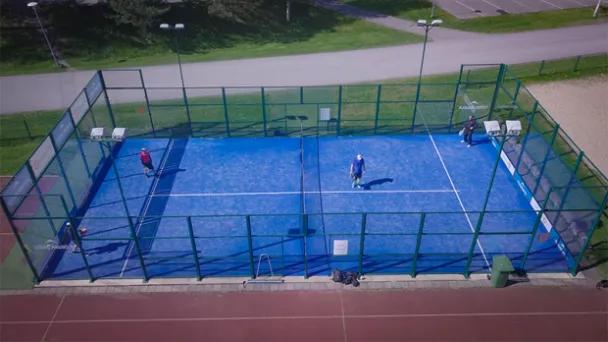 Sininen padel-kenttä, neljä pelaajaa, kirkas päivä.