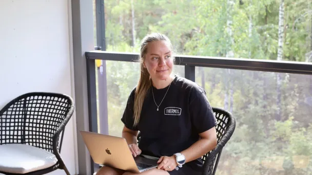 Nainen istuu terassilla ja käyttää kannettavaa tietokonetta.