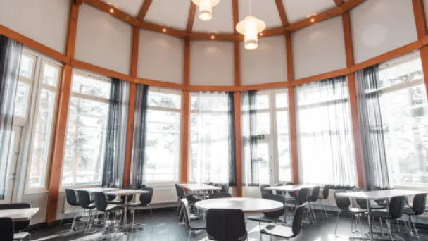 Pyöreä huone suurella ikkunaseinällä ja valaisimilla, tyhjiä pöytiä ja tuoleja.