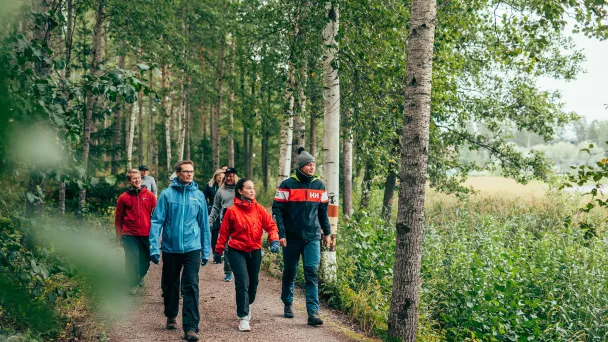 Ryhmä ihmisiä kävelee metsäpolulla kesäpäivänä.