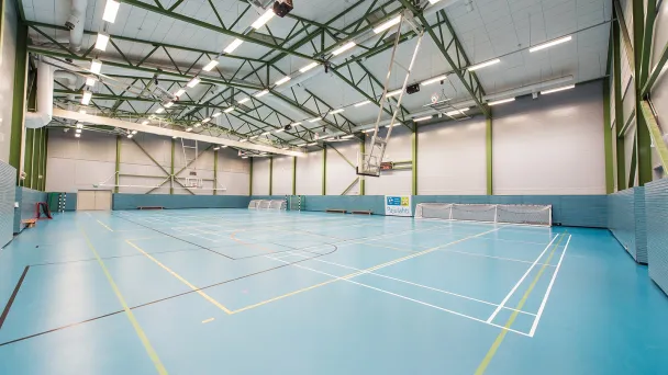 Tyhjä liikuntahalli, vaaleansiniset lattiat, koripallokorit, kattovalot.