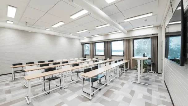 Valoisa luokkahuone, jossa on riveittäin pöytiä ja tuoleja.