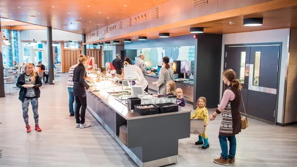 Valoisassa ravintolassa ihmisiä buffetin äärellä, lapset ja aikuiset ruokailemassa.