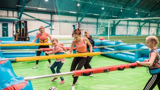 Aikuiset ja lapset pelaavat ihmisfutista sisähallissa.