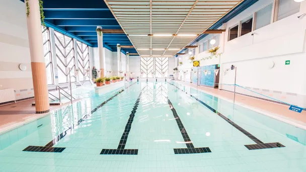 Sisäuima-allas, vaaleansininen vesi, valaistus, ja raidat pohjassa.