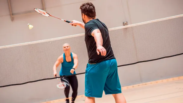 Kaksi henkilöä pelaamassa sulkapalloa sisähallissa.