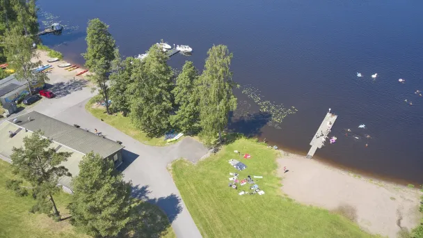 Ilmakuva rannasta, jossa ihmisiä nurmikolla ja laituri järvelle.