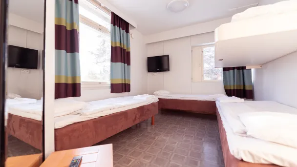 Hostellihuone, jossa kaksi sänkyä ja kerrossänky, kirkas valaistus.