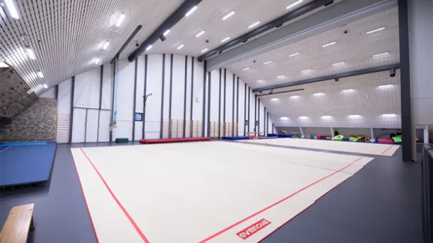 Voimistelusali, jossa on suuri vaalea matto ja korkea katto.