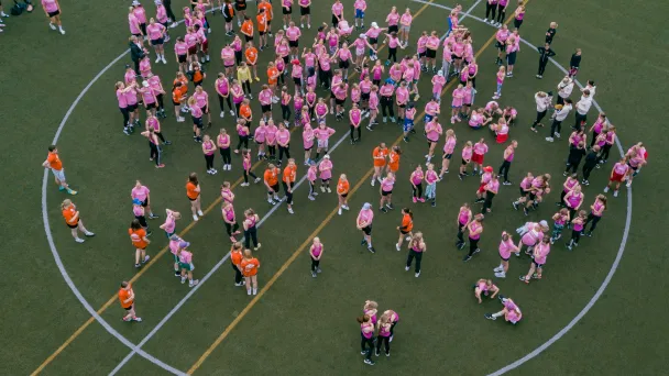 Crowd of people in pink and orange shirts on a sports field.