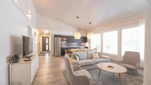 Valoisa olohuone ja keittiö avarassa hirsitalossa, vaaleat kalusteet ja isot ikkunat.