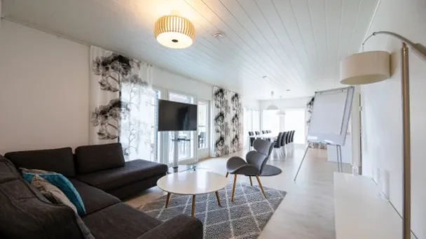 Tilava, vaalea olohuone, jossa sohva, televisio, lepotuolit ja pöytä.