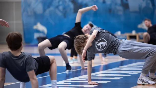 Nuoret harjoittelevat voimistelusalissa sinisellä alustalla.