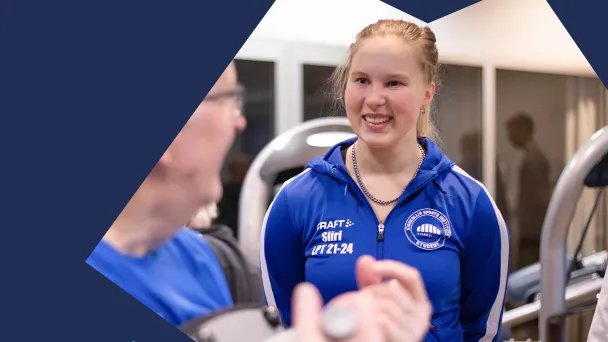 Punahiuksinen nainen sinisessä urheiluvaatteessa hymyilee kuntosalilla.