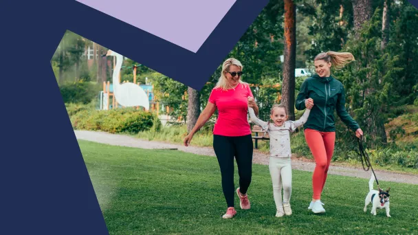 Mummo, lapsi ja äiti kävelevät käsi kädessä Pajulahden rannalla ja pieni koira kulkee heidän vierellään hihnassa.