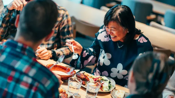 Ihmiset nauttivat ateriasta ravintolassa ja hymyilevät.