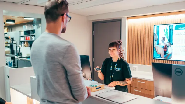 Asiakaspalvelija keskustelee asiakkaan kanssa vastaanottotiskillä.