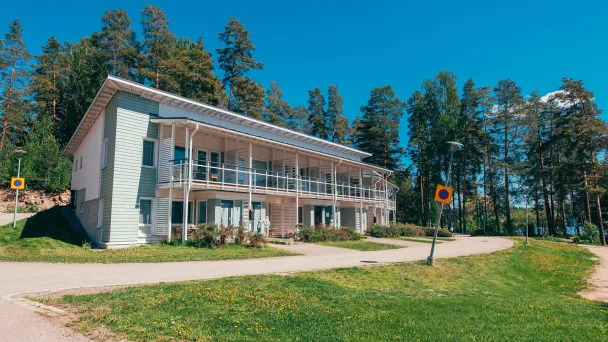 Kaksikerroksinen talo mäntymetsän edessä aurinkoisella päivällä.