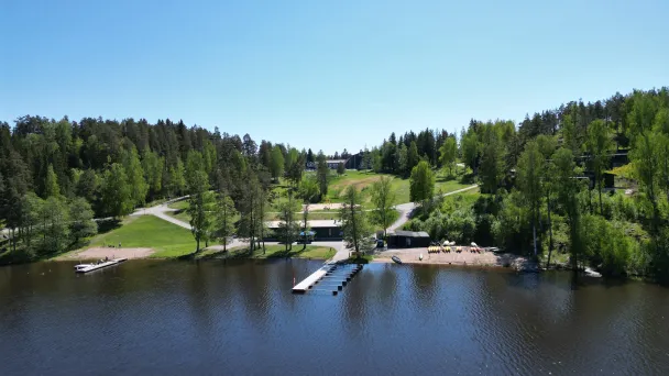 Järvimaisema laiturilla, vihreää metsää taustalla, sininen taivas.