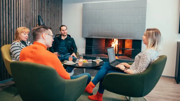 Neljä ihmistä kokoustaa takkatulen äärellä kannetavat tietokoneet sylissä.