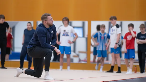 Urheilun asiantuntija kouluttamassa fysiikkaharjoitteita yläkoululeirityksen oppilaille