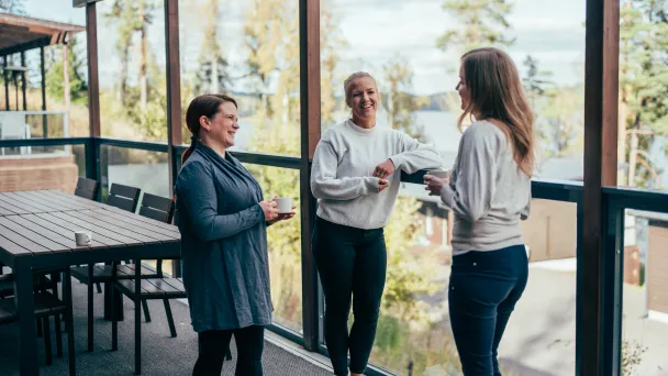 Kolme naista juttelee Villa Kallion terassilla, jossa on järvinäköala.