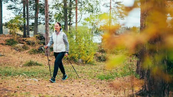 Naisen sauvakävelee syksyisessä metsässä.