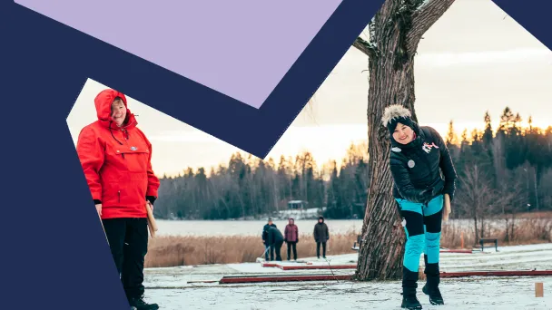 Kaksi iloista naista pelaa mölkkyä lumisella maalla.