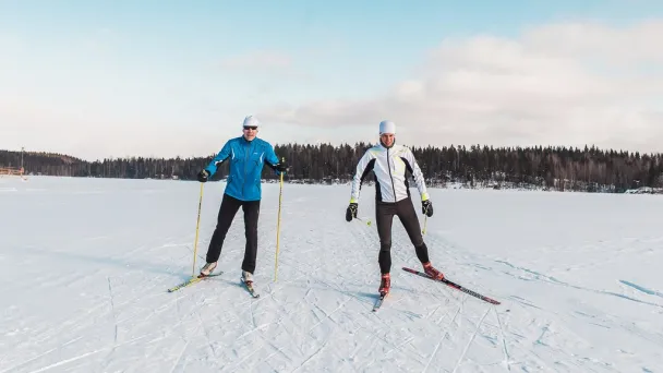 Kaksi ihmistä hiihtää lumisella järvellä aurinkoisena päivänä.