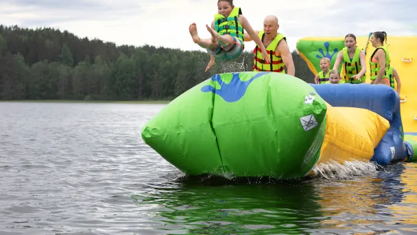 Lapsi hyppää ilmapatjalta järveen muiden katsoessa taustalla.