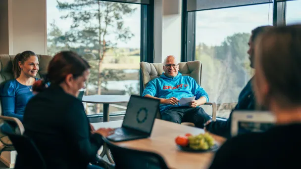 Ihmiset työskentelevät Omenatarhan kokoustilassa läppäreillä ja ikkunoista avautuu järvi- ja metsänäkymä.