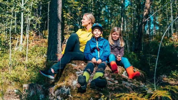 Perhe istuu kivellä syksyisessä metsässä