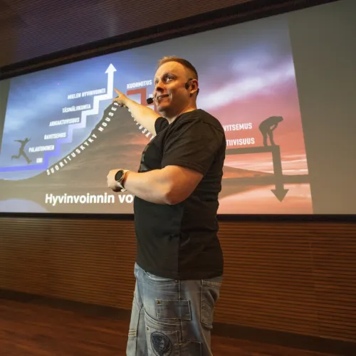 Mies esittelee diaa auditoriossa, värikäs tausta.