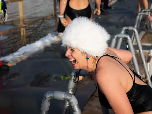 Naurava nainen jäisessä vedessä, pukeutunut mustaan uimapukuun ja valkoiseen hattuun.