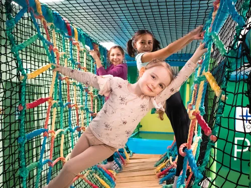 Lapset leikkivät värikkäällä kiipeilyverkolla sisätiloissa.