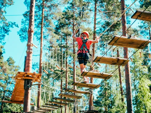 Person navigating a ropes course in a forest, wearing safety gear.