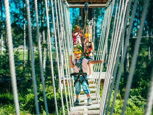 Kaksi lasta seikkailee köysiradalla metsässä.
