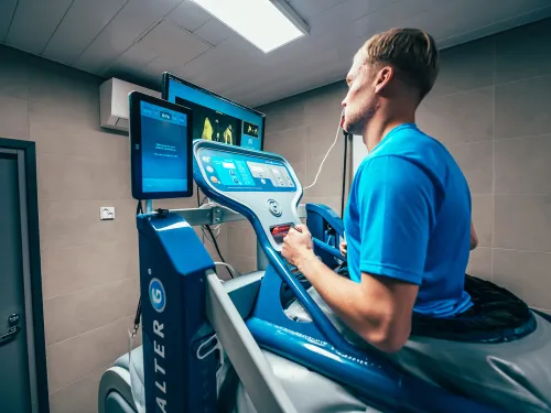 Mies juoksee kuntolaitteella kuntosalilla tarkkaillen näyttöä.
