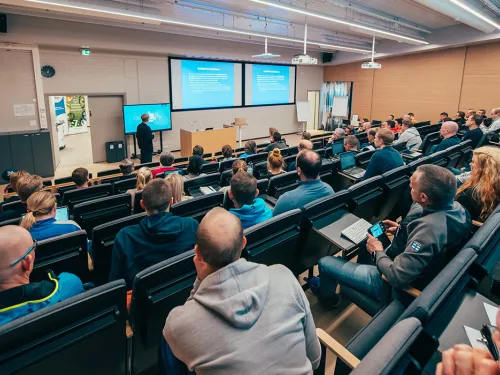 Lecture hall with audience facing a speaker and projected slides.