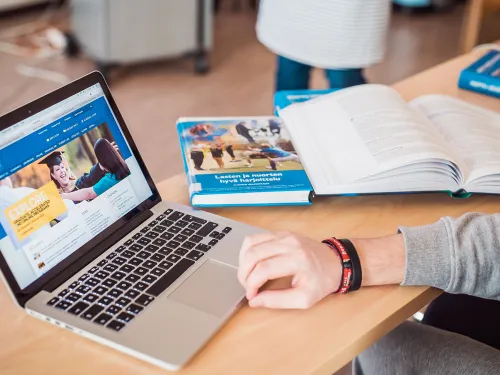 Laptop and open book on a desk, person working.