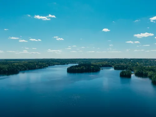 Aerial view of a calm blue lake under a clear sky with scattered small clouds.