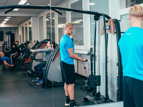 Mies treenaa kuntosalilla peilin edessä.